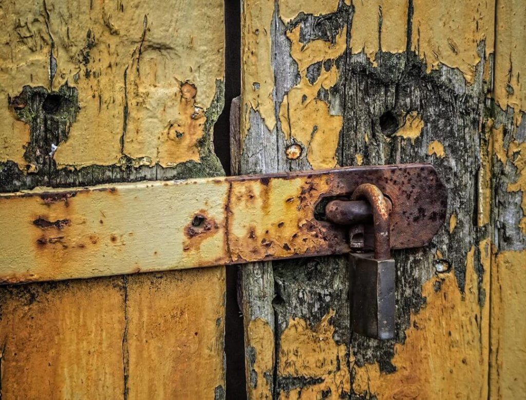 Uma porta antiga, amarela, com cadeado enferrujado